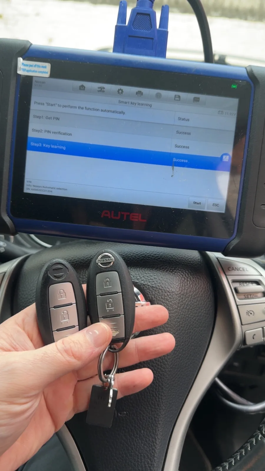 Two coded smart keys held in front of an Autel key programmer inside a vehicle