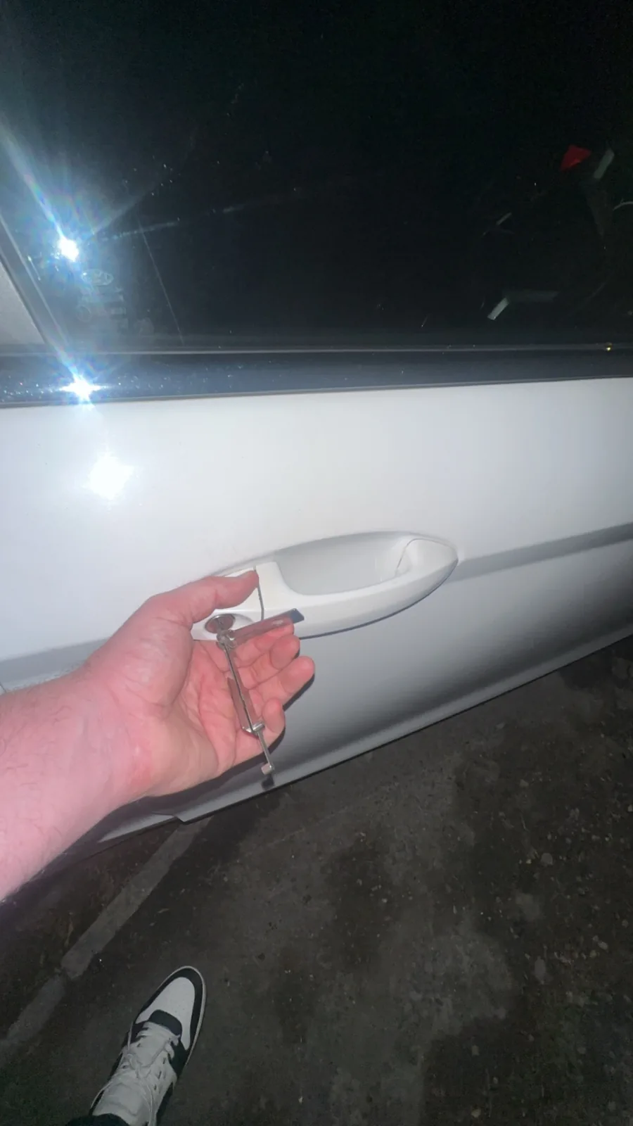 Freshly cut spare car key held next to a silver car door in Derby