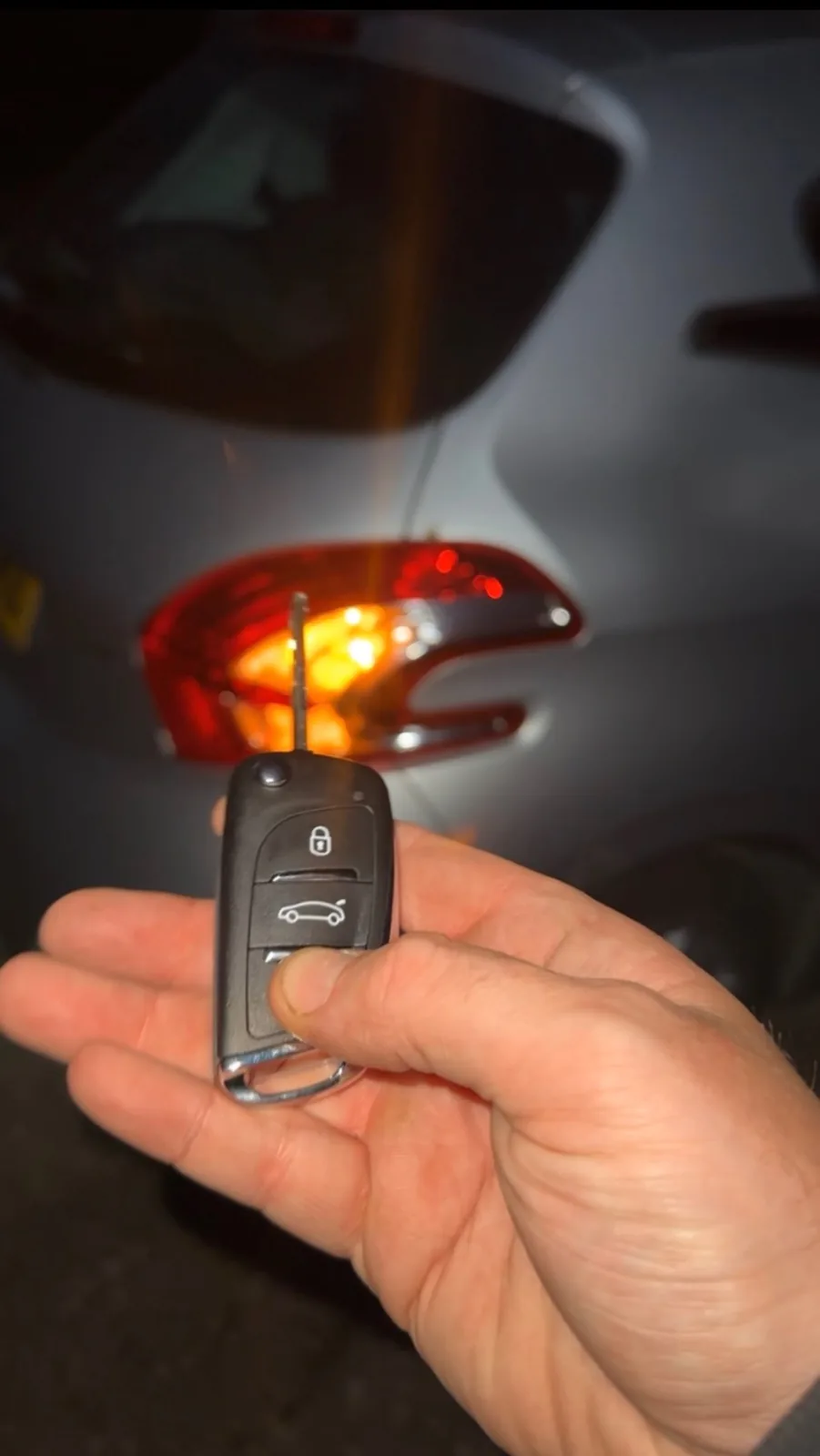 Newly programmed key testing hazard lights on a white car at night