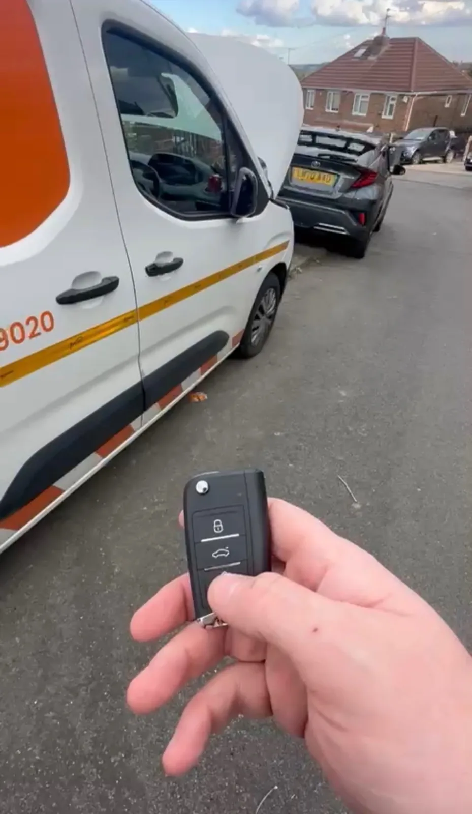 Van remote key held beside a white and orange commercial van after key replacement