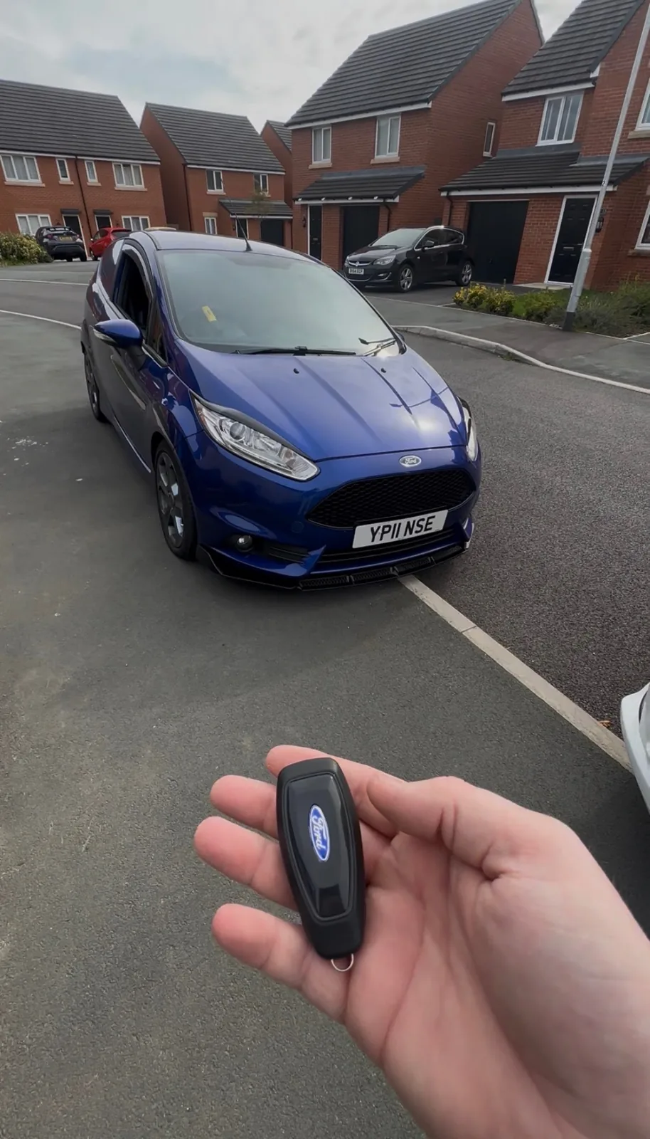 New Ford key held in front of a blue Ford Fiesta ST on a Derby driveway
