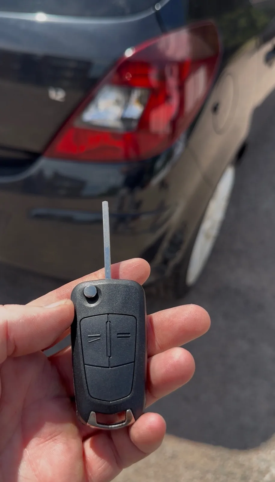 Newly cut flip key held behind a grey hatchback on a Derby street